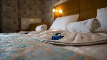 A neatly made bed with rolled towels and a blue bottle, suggesting a hotel room setting.