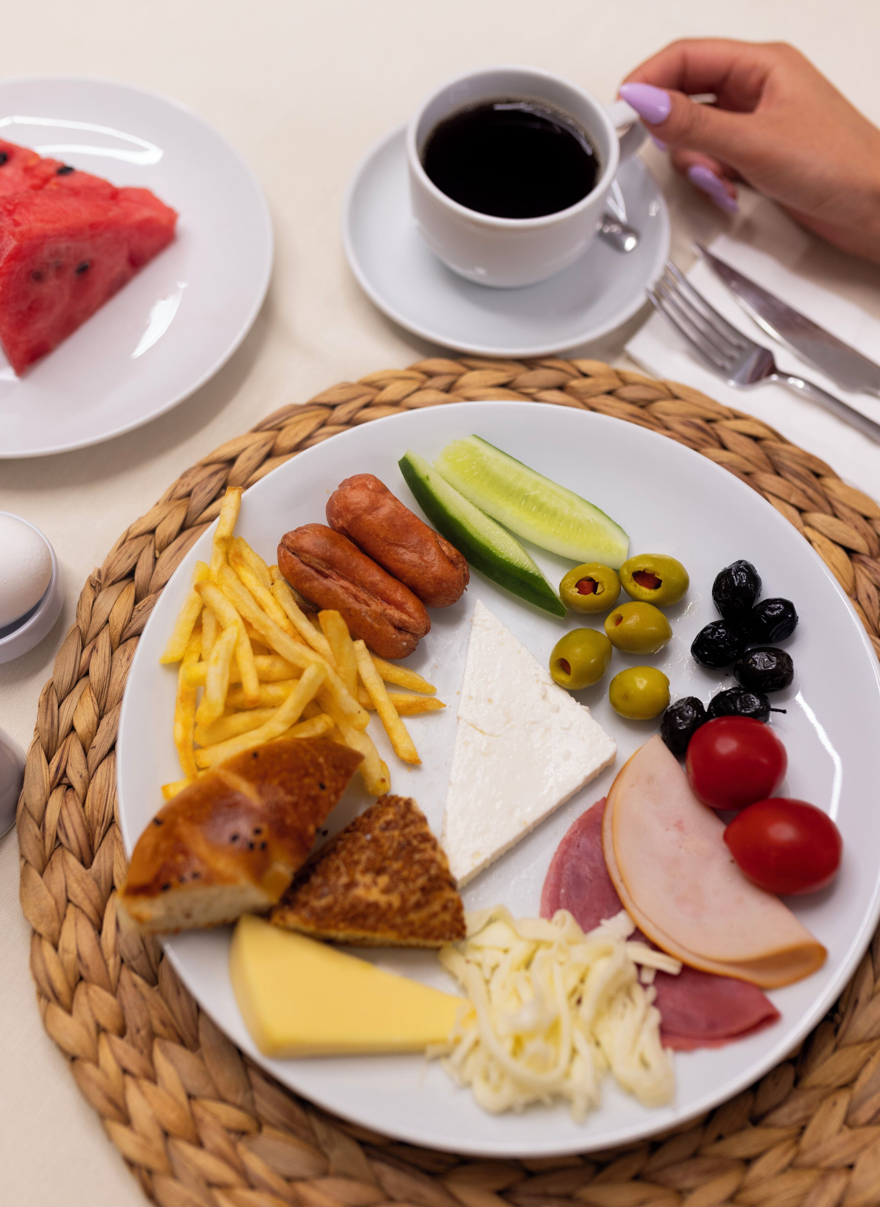 A plate with various foods including cheese, ham, olives, cucumbers, and fries.