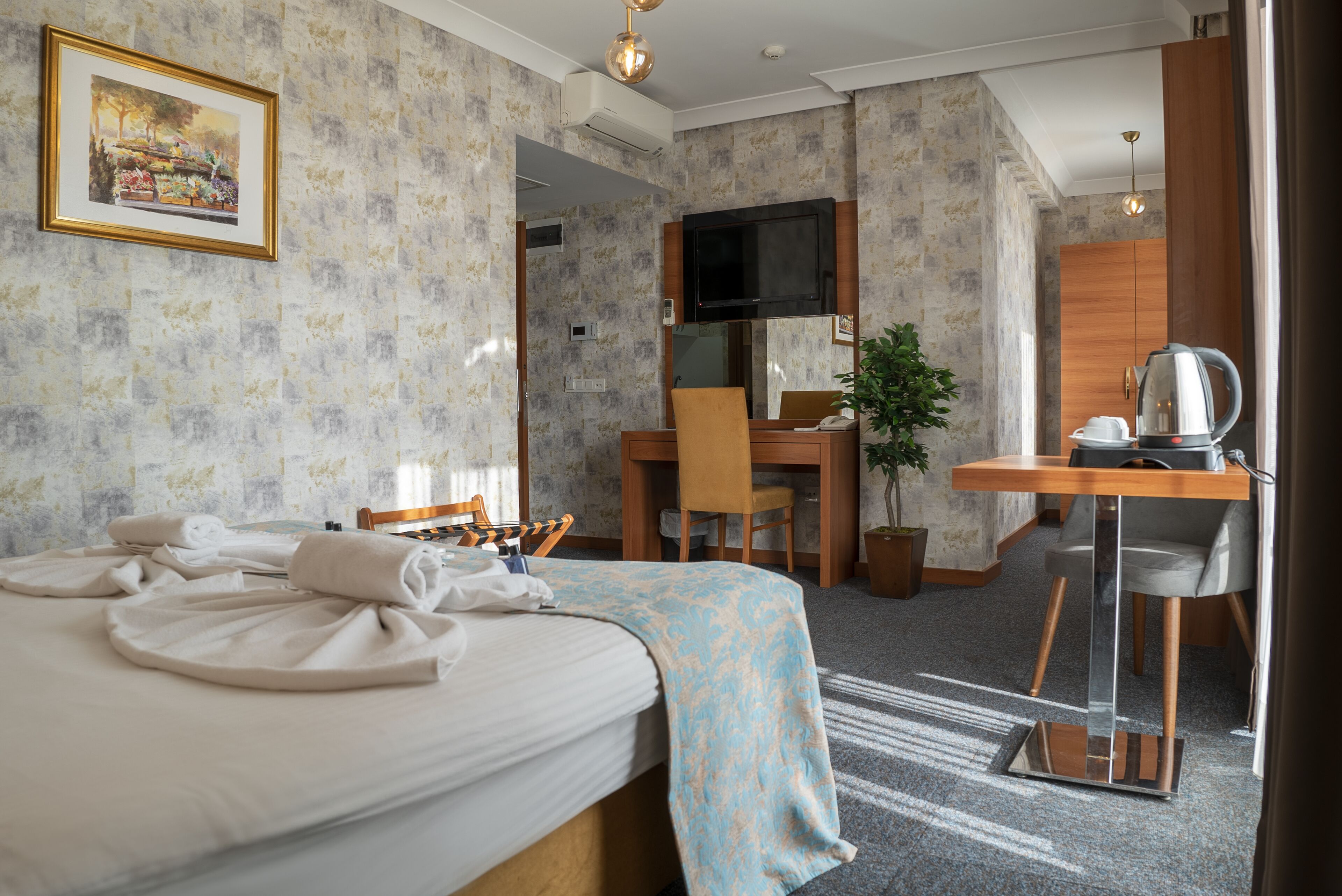 A hotel room with a bed, a desk, a chair, a television, and a plant.
