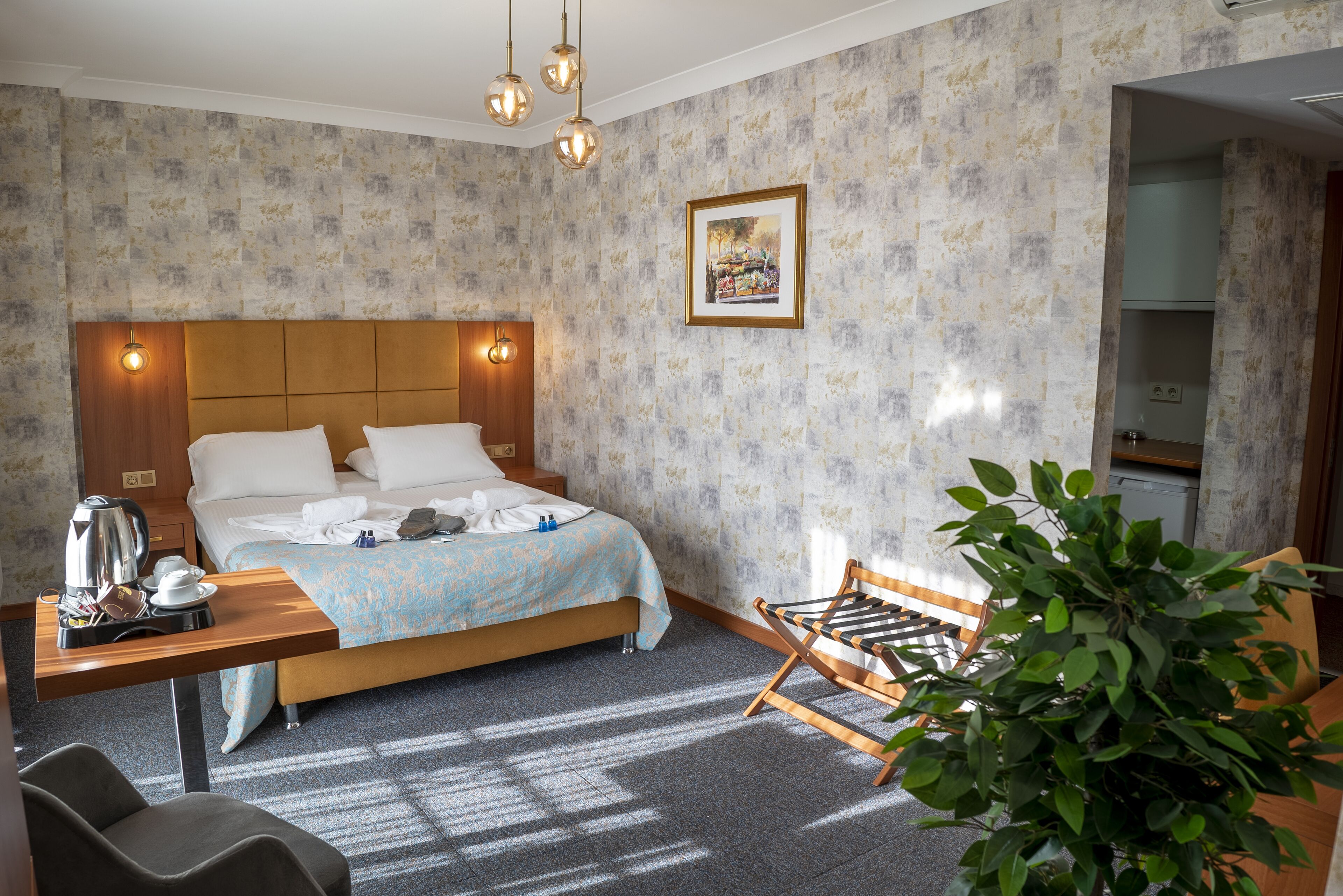 Habitación de hotel con cama, mesita de noche, silla y una planta en maceta.