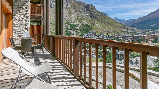 A wooden deck with a stone wall, a table, and two chairs. - Luxury chalet with sauna, fireplace and WiFi in Val-d'Isère (Val-d'Isère)