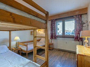 A bunk bed room with a wooden ladder, a bedside table with a lamp, a window with curtains, and a radiator.
