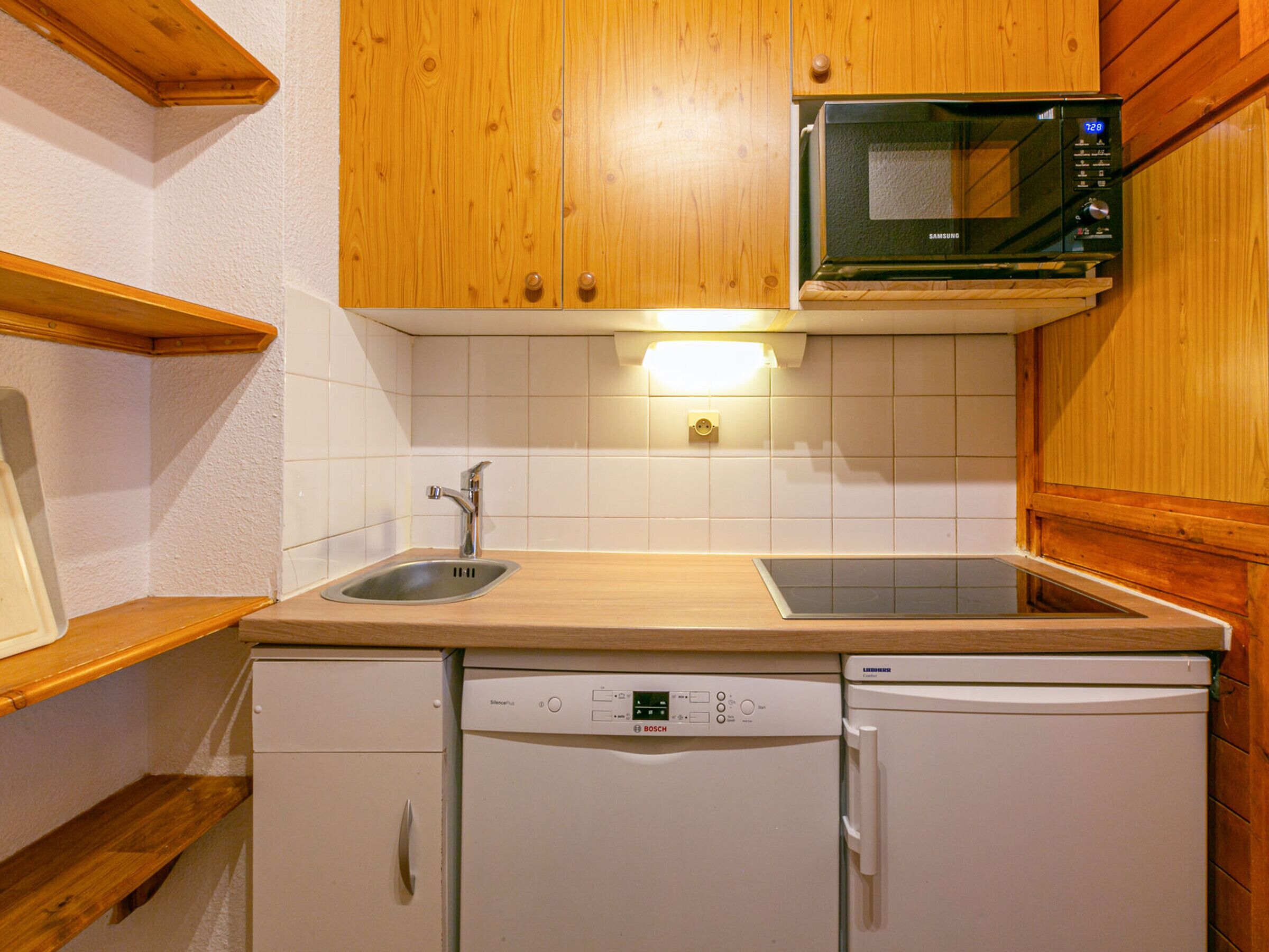 A compact kitchen with wooden cabinets, a stainless steel sink, a Bosch dishwasher, and a microwave.