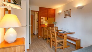 Habitación pequeña con una mesa de comedor, sillas, un banco, un televisor montado en la pared y una lámpara sobre un mueble.