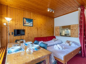 A wooden-paneled room with a bed, a table set for two, a television, and a painting on the wall.