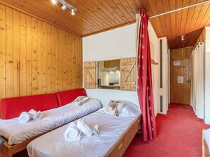 A room with wooden walls, a red carpet, two beds with white linens, and a red curtain.