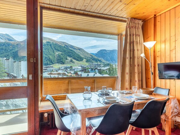 A dining area with a table set for four, a TV mounted on the wall, and a view of a mountainous landscape.