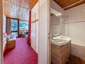 A hotel room with a wooden ceiling, a large window with a view of a snowy landscape, a wooden cabinet with a sink, and a red carpeted floor.