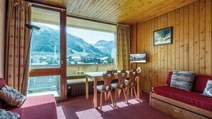 Une pièce chaleureuse avec un plafond en bois, un canapé rouge, une table en bois avec des chaises et une grande fenêtre donnant sur une vue imprenable sur les montagnes.