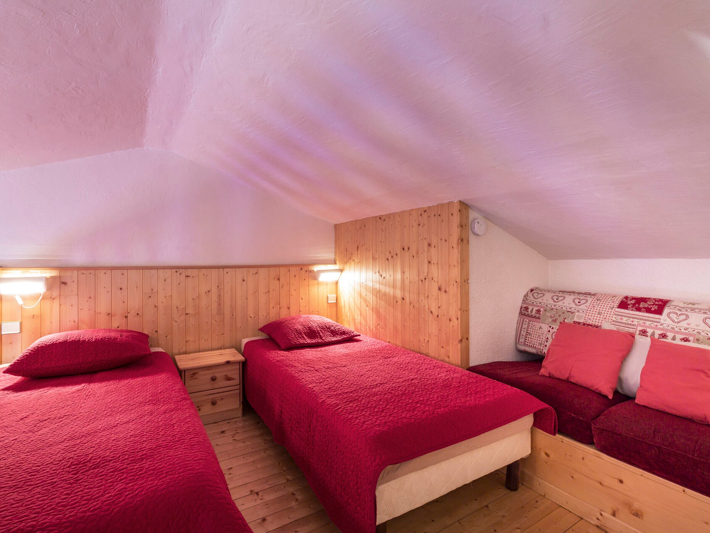 A cozy room with two beds, wooden walls, and a sloped ceiling.
