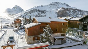 A snow-covered mountain town with wooden buildings, a ski lift, and a clear view of the mountains.