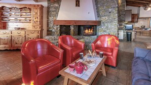 A cozy living room with a stone fireplace, leather chairs, and a wooden table with a teapot and cups.