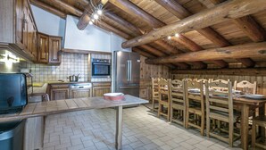 A rustic kitchen with wooden beams, a tiled backsplash, and a dining area with wooden chairs and a table.