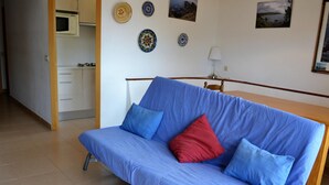 Une pièce avec un canapé bleu, une table en bois et un coin cuisine à l’arrière-plan.