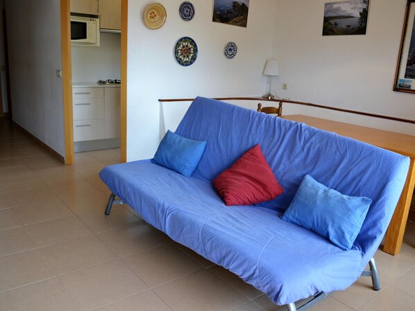 A room with a blue sofa, a wooden table, and a kitchen area in the background. - Family ground floor in Cap de Ras, pets allowed (Llançà)
