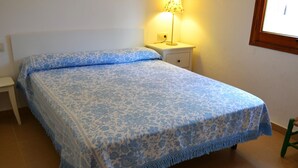 Un lit recouvert d’une couvre-lit à motifs floraux bleus, une table de chevet avec une lampe et une fenêtre avec un cadre en bois.