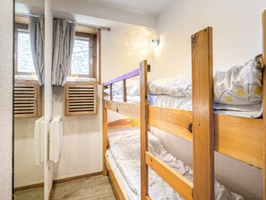 A dormitory room with bunk beds, a window with curtains, a radiator, and a wall-mounted light fixture.
