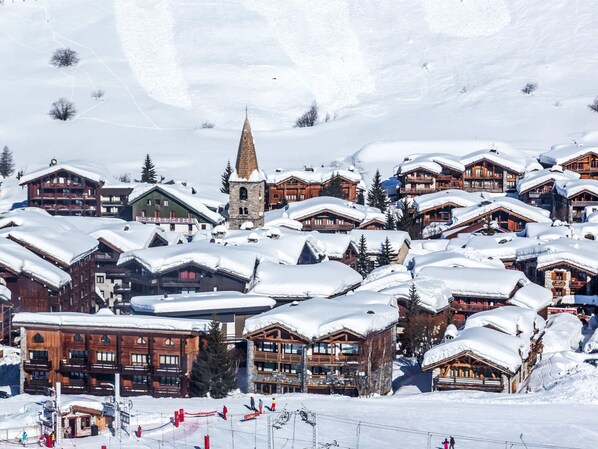 A snow-covered village with wooden buildings, a church spire, and ski slopes.