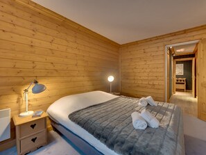 A wooden-paneled room with a bed, bedside lamp, and a nightstand with drawers.