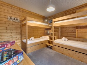 A bunk bed room with wooden walls, a ceiling light, and a table with a board game.