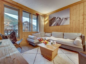 A cozy living room with a sofa, a wooden coffee table, and a view of a mountain landscape through large windows.
