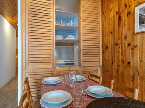 A dining area with a table set for four, wooden shutters, and a view of the kitchen.