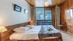 Un dormitorio con paneles de madera, una cama, una lámpara de lectura, una silla y una ventana con cortinas.
