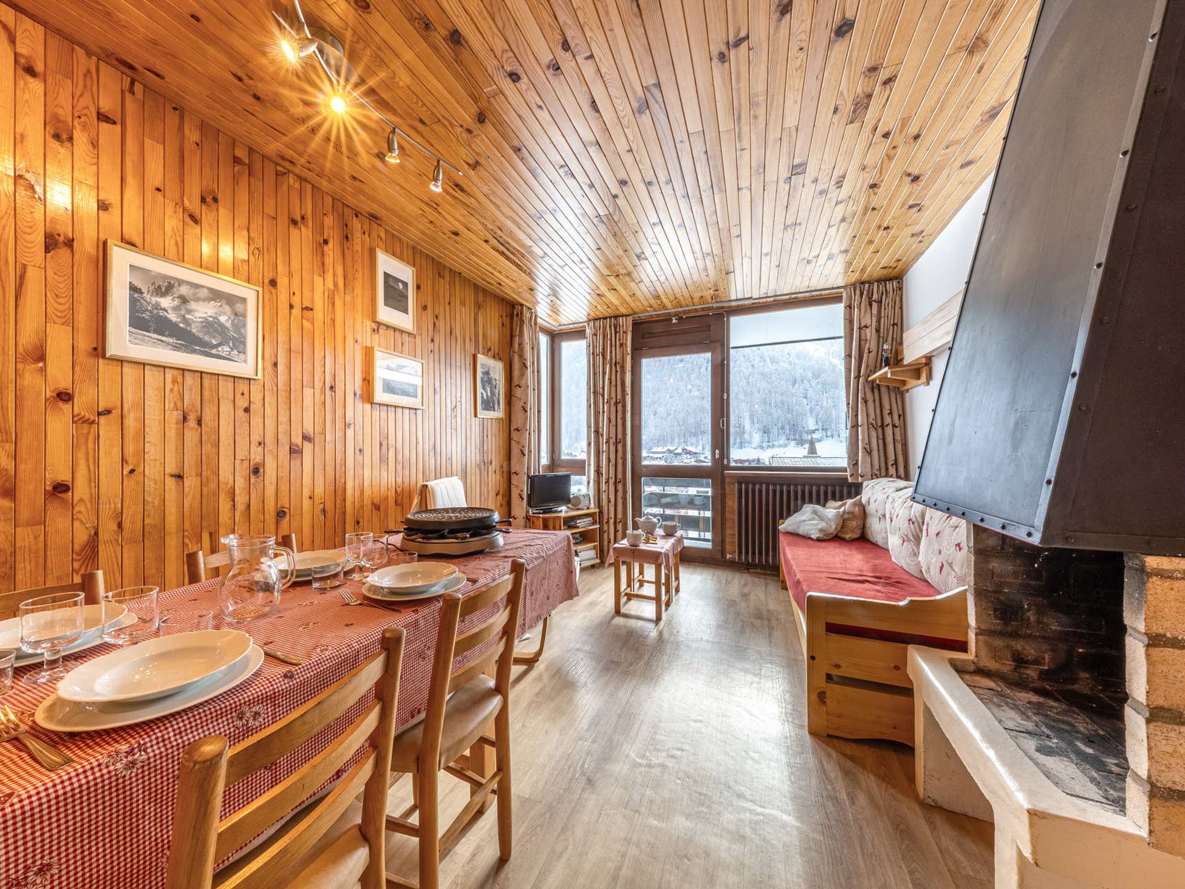 A wooden interior with a dining table set for four, a sofa, and a fireplace.