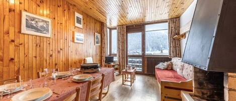 A wooden interior with a dining table set for four, a sofa, and a fireplace.