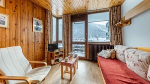 Una habitación acogedora con paredes y techo de madera, un sofá, una silla, una mesita y un televisor.