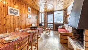 Un interior de madera con una mesa de comedor preparada para cuatro personas, un sofá y una chimenea.