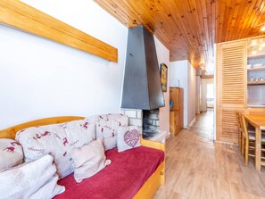 A cozy room with a wooden ceiling, a fireplace, a sofa with patterned cushions, and a dining area with wooden furniture.