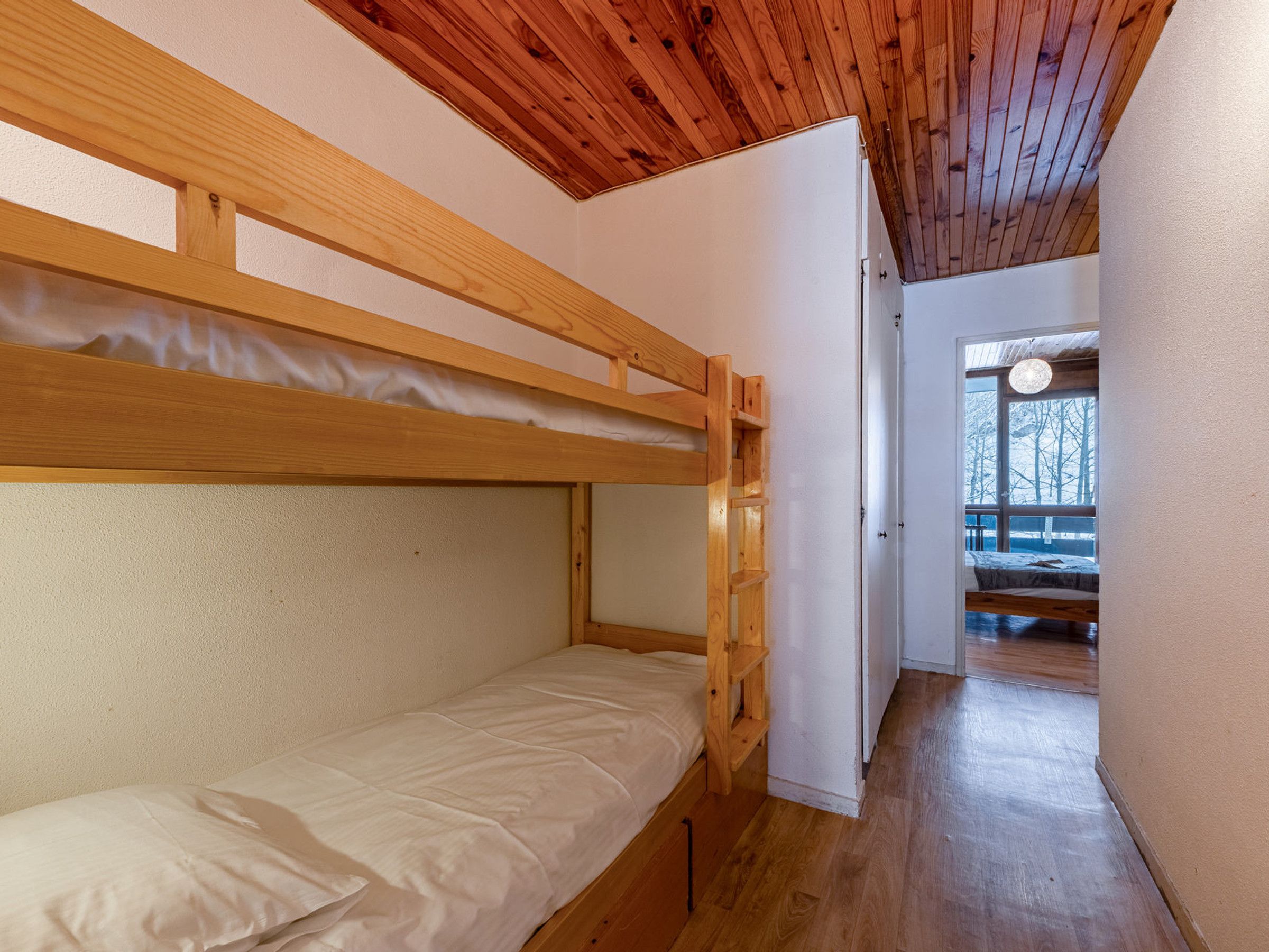 A bunk bed room with a wooden ceiling and a view of a snowy landscape through a window.