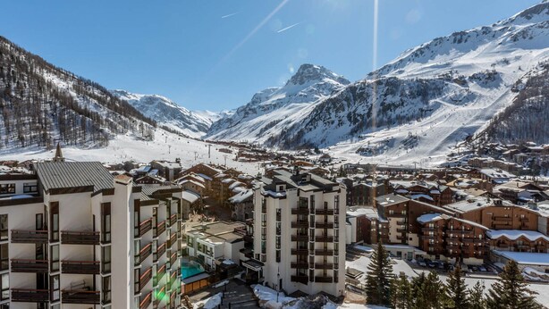 Un pueblo nevado en la montaña con edificios modernos, incluyendo un hotel con balcones y una zona de piscina.