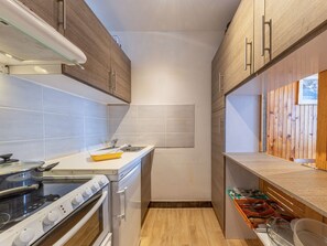 A compact kitchen with a stove, oven, and sink. It features wooden cabinets, a tiled backsplash, and a wooden countertop with a dish rack.