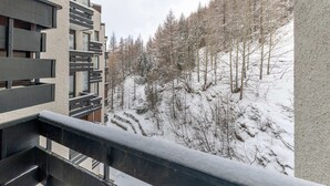 Un edificio moderno con un balcón que da a una ladera nevada con árboles.