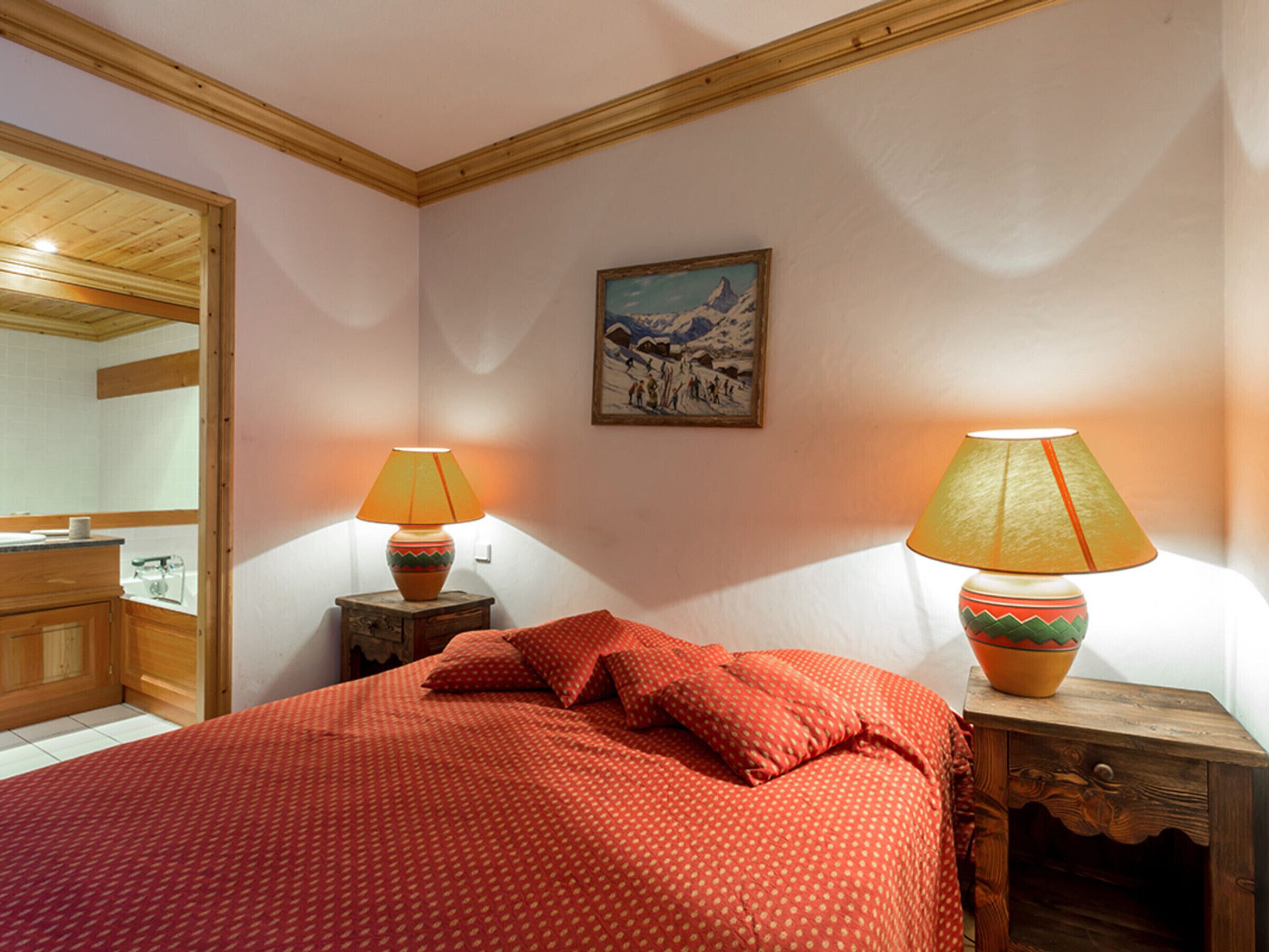 Ein Schlafzimmer mit einem Bett, zwei Nachttischlampen, einem Holznachttisch, einem Spiegel und einem Bild an der Wand.