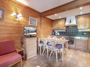 A cozy wooden cabin interior with a dining area, kitchen, and a television displaying a snowy landscape. - Cozy Apartment with Warm Tones, WiFi, and Balcony in La Roche des Fours Residence (Val-d'Isère)