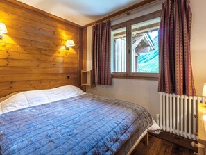 A cozy wooden room with a bed, a window with curtains, and a radiator. - Cozy Apartment with Warm Tones, WiFi, and Balcony in La Roche des Fours Residence (Val-d'Isère)