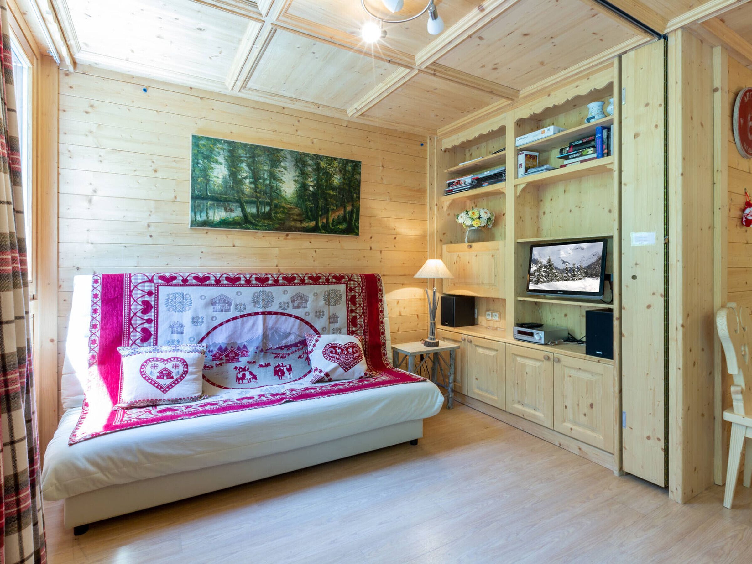 A wooden room with a bed, a television, and a bookshelf.
