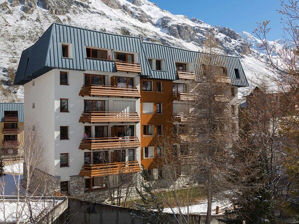 A multi-story building with balconies, set against a snowy mountainous backdrop.