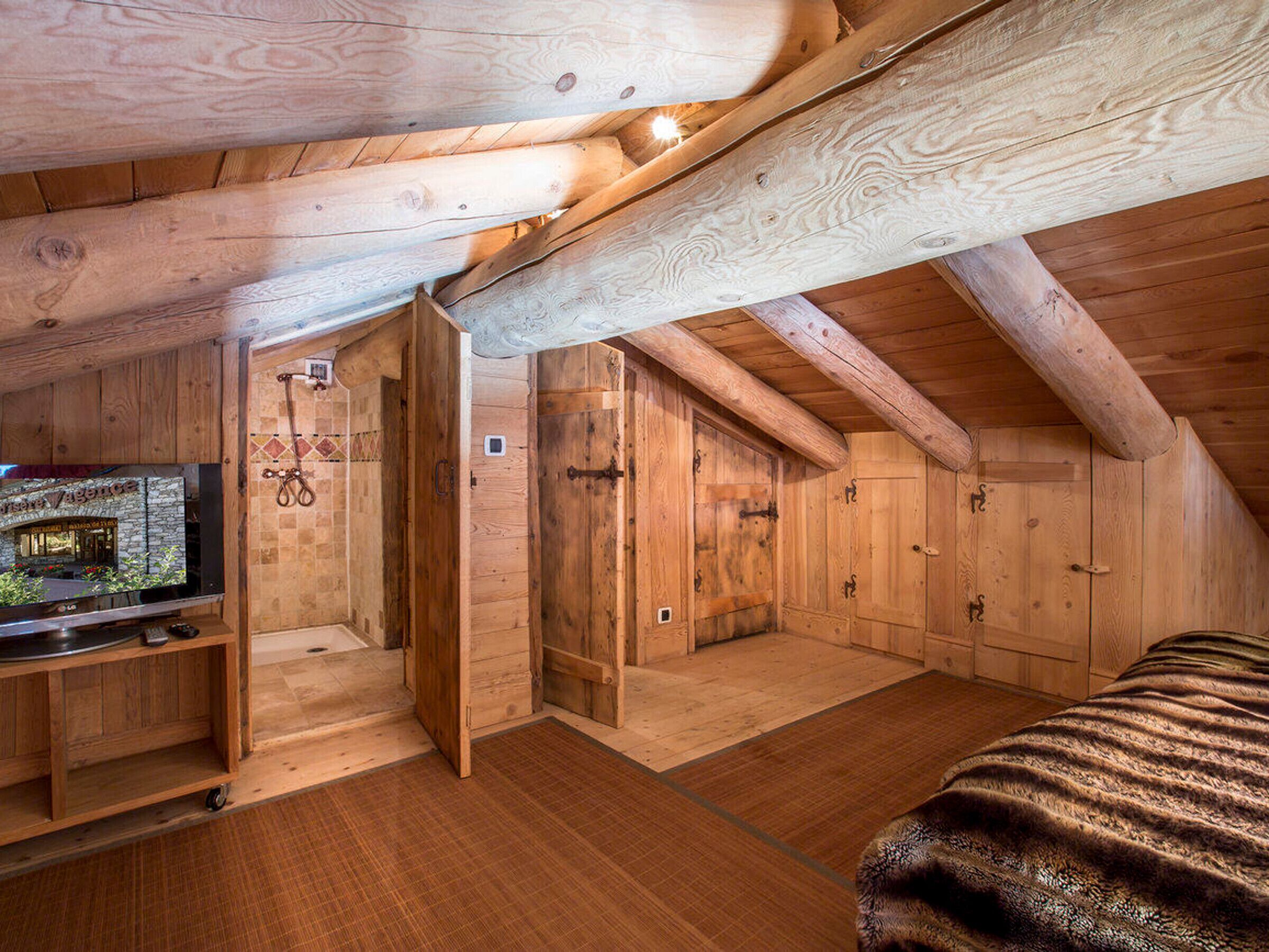 A wooden attic bedroom with a television on a wooden stand, a bed, and a small bathroom with a shower.