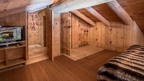 Ein Schlafzimmer im Dachgeschoss mit Holzboden, einem Fernseher auf einem Holzständer, einem Bett und einem kleinen Badezimmer mit Dusche.