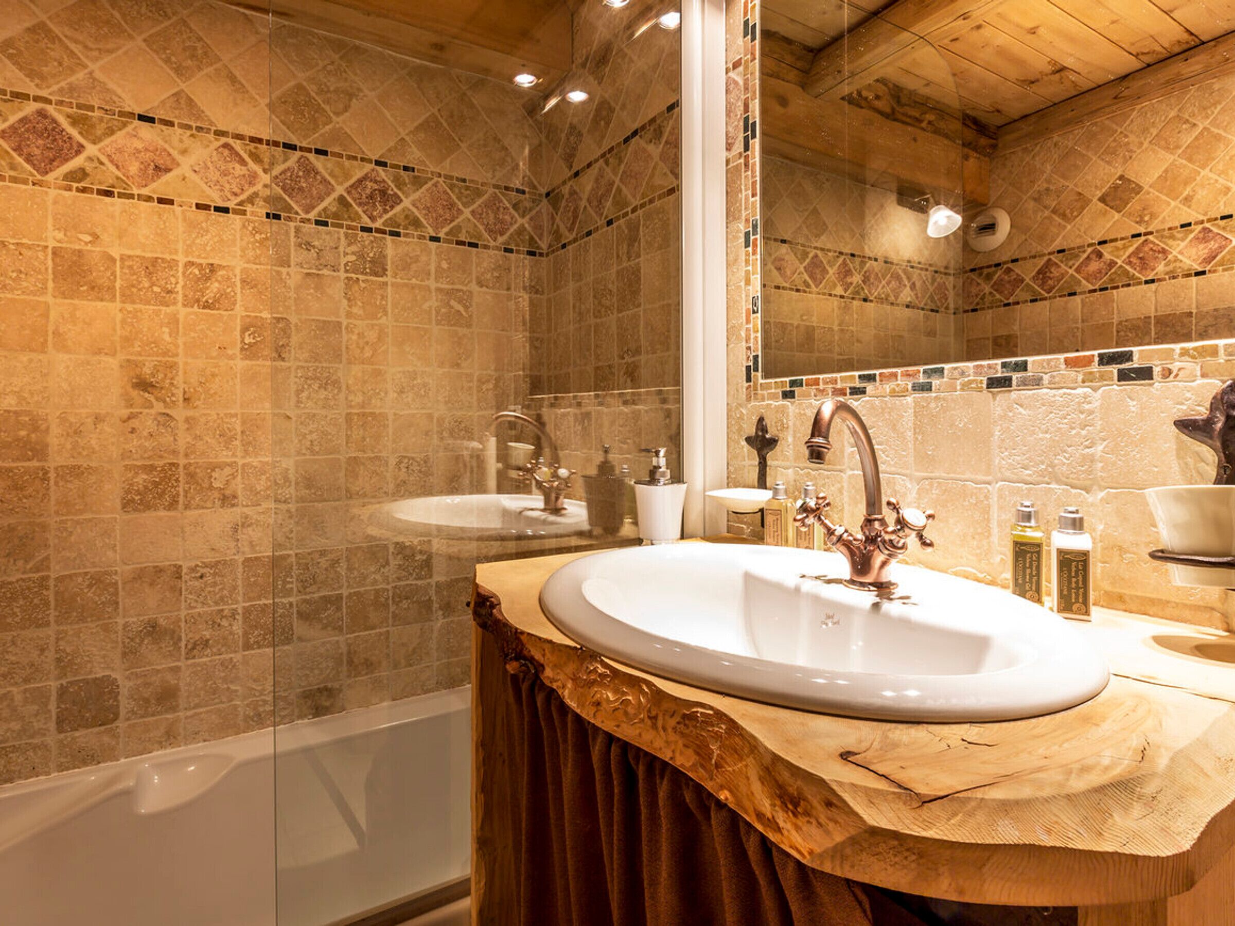 A bathroom with a large mirror, two sinks, a bathtub, and a wooden vanity.