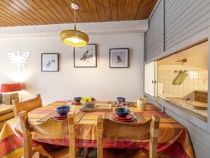 A dining area with a wooden table set for four, surrounded by chairs, with a hanging light fixture above. - Charming Apartment with South-Facing Balcony in Heart of Resort, Near Ski Slopes (Val-d'Isère)