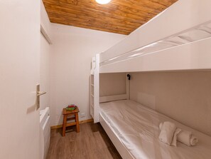 A bunk bed room with a wooden ceiling, a small wooden stool, and a white wall.