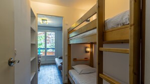 A compact room with bunk beds, a small table, and a window with a view of greenery.