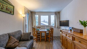 Ein gemütliches Wohnzimmer mit einer Couch, einem Esstisch mit Stühlen, einem Fernseher und einem Holzschrank.
