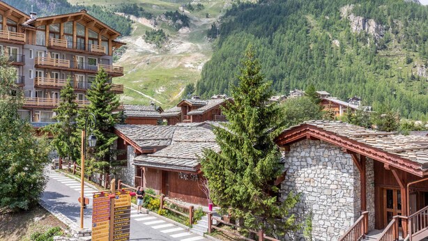 Ein Bergresort mit Holzbauten, Steinarchitektur und Blick auf ein Gebirge.
