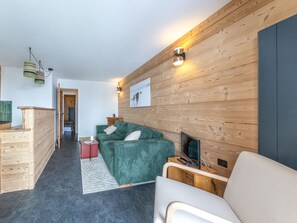 Una sala moderna con un sofá verde, una mesa de centro de madera y un televisor de pantalla plana. Se observa un revestimiento de pared de madera y una chimenea.